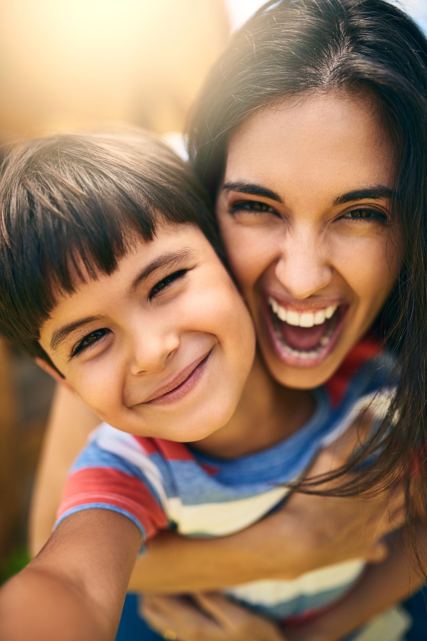 Laughing mother and young son cheek to cheek outdoors
