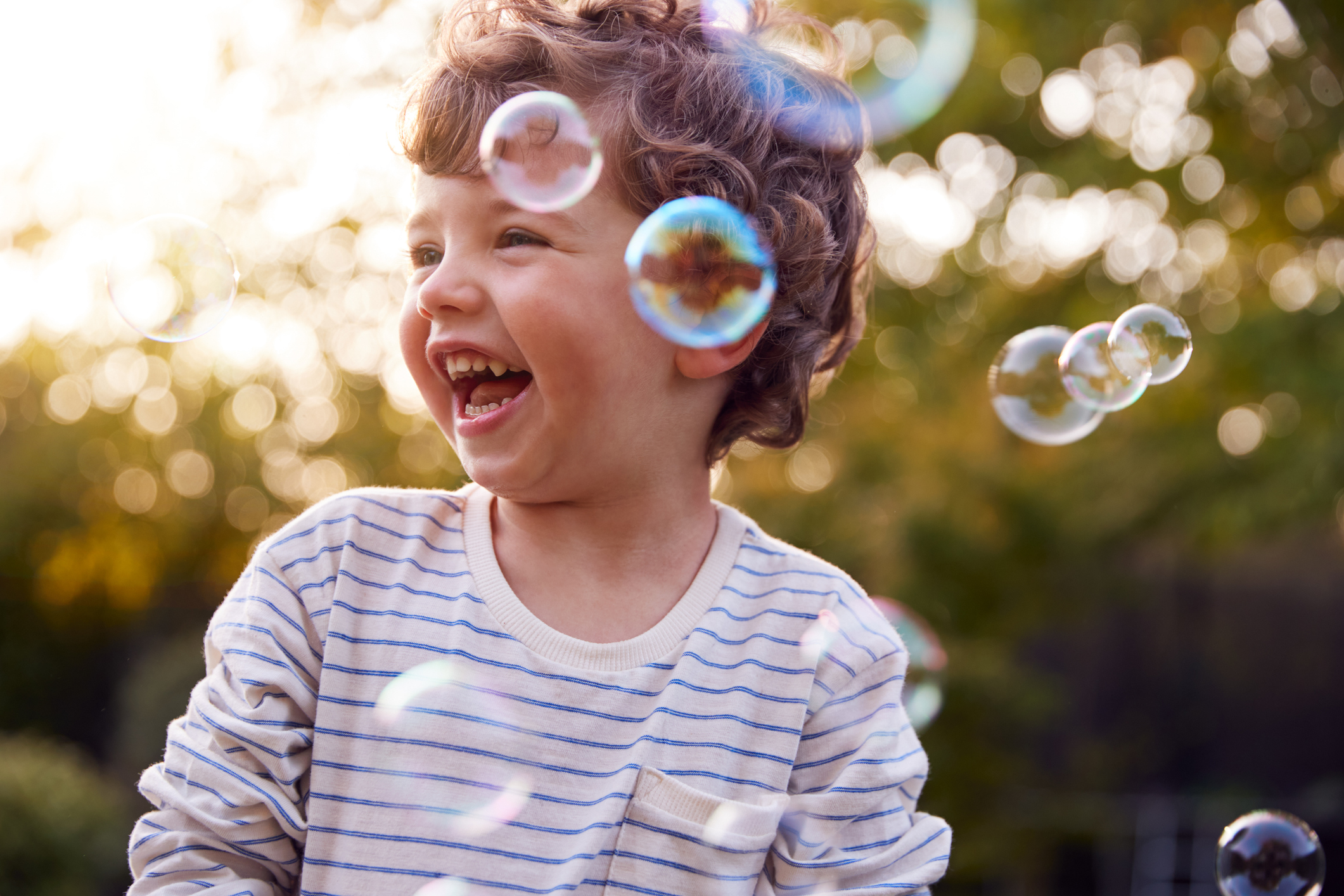 Happy laughing boy playing with bubbles outdoors