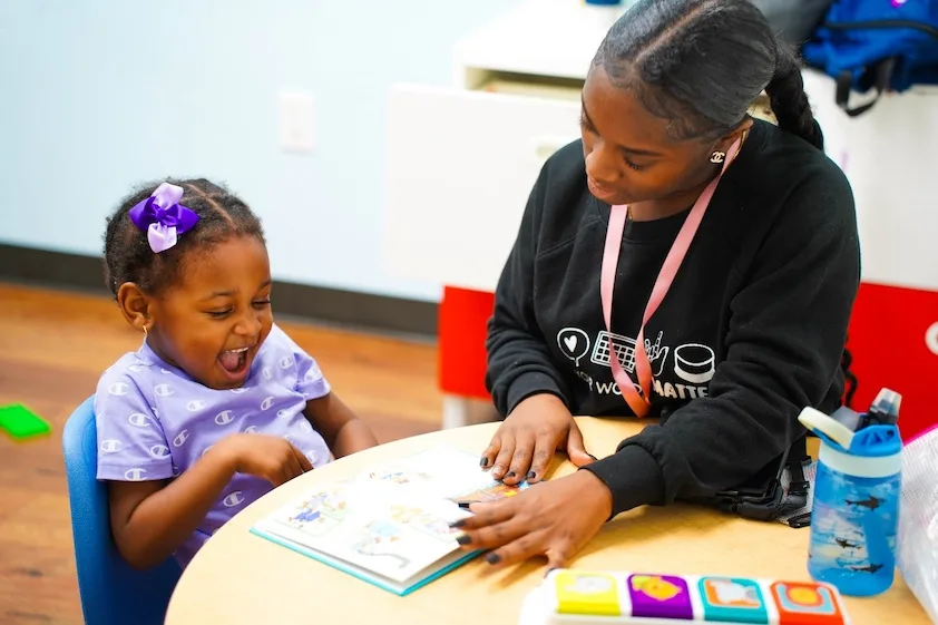 a woman wearing a lanyard that says i work matte is reading a book to a little girl