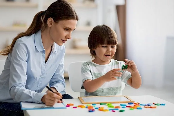 a woman is sitting at a table with a child who is playing with letters