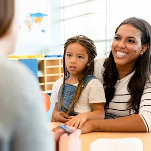a woman and a little girl are sitting at a table talking to a teacher