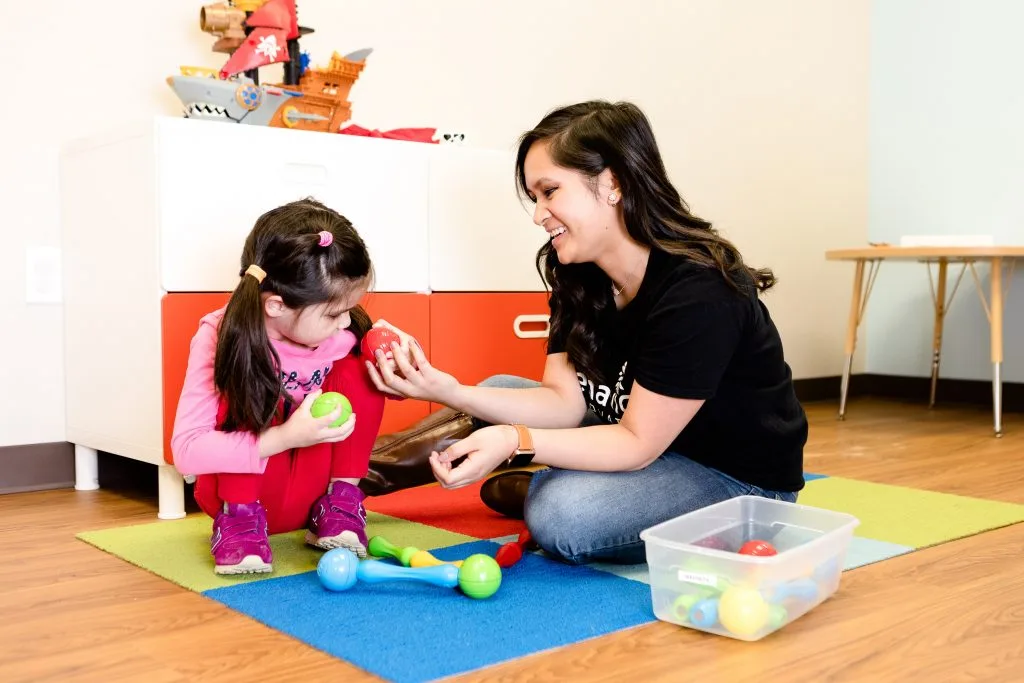 a woman in a black t-shirt with the letter a on it is playing with a little girl
