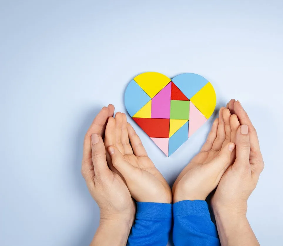 World autism awareness day concept. Woman and child hands holding puzzle heart on light blue background. Top view