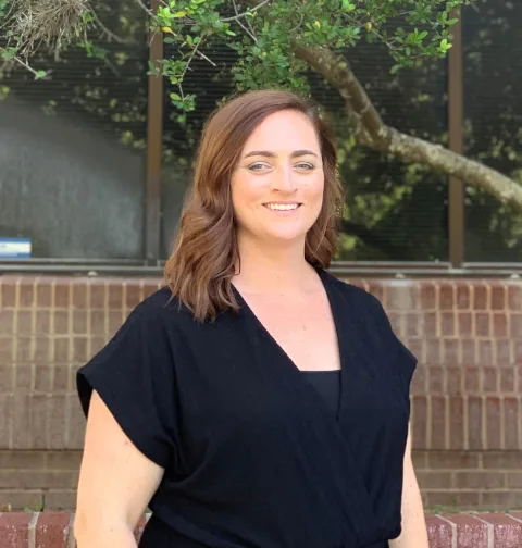 a woman in a black shirt smiles in front of a building