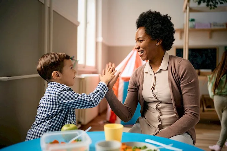 a woman is giving a child a high five while sitting at a table