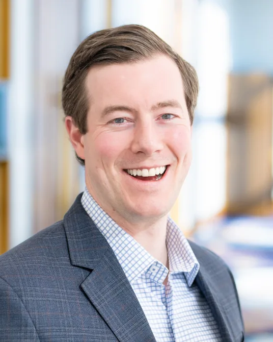a man in a suit and plaid shirt smiles for the camera
