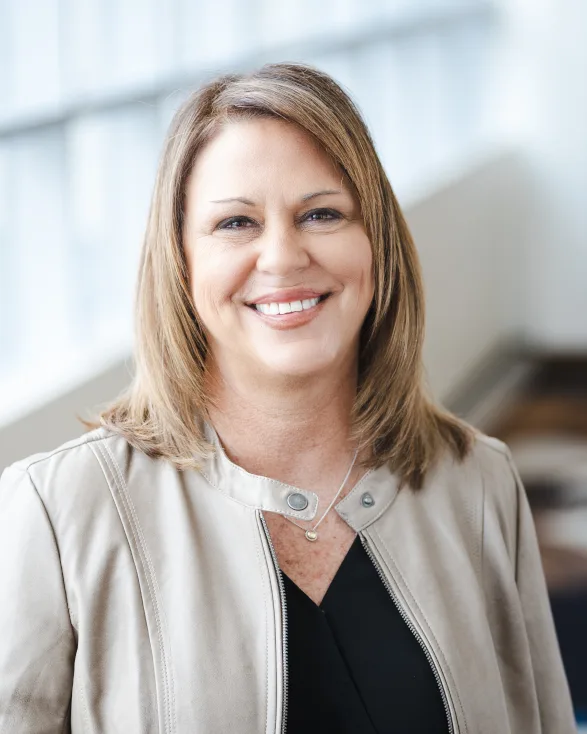 a woman wearing a black shirt and a tan jacket smiles for the camera