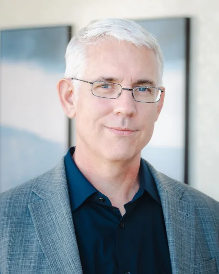 a man wearing glasses and a suit smiles for the camera