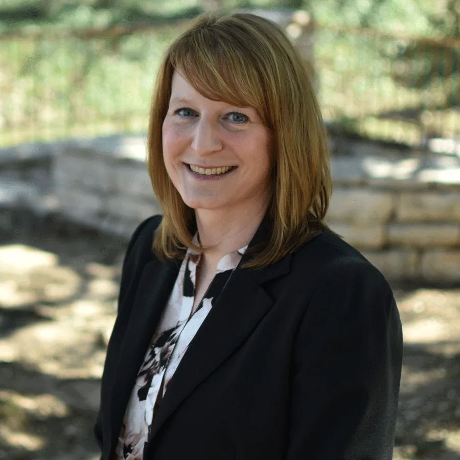 a woman in a black jacket and floral shirt smiles for the camera