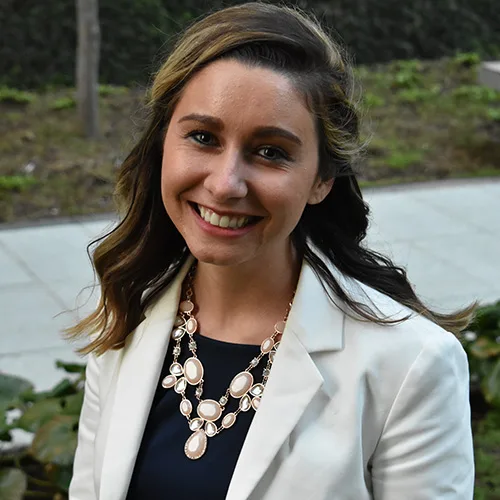 a woman wearing a white jacket and a necklace smiles for the camera