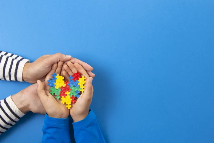 World autism awareness day concept. Adult and child hands holding puzzle heart on light blue background