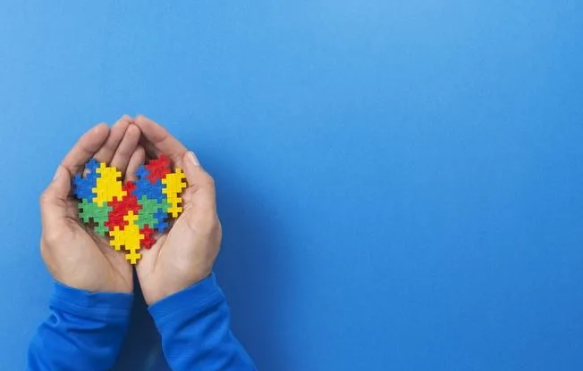 World autism awareness day concept. Child hands holding colorful puzzle heart on blue background