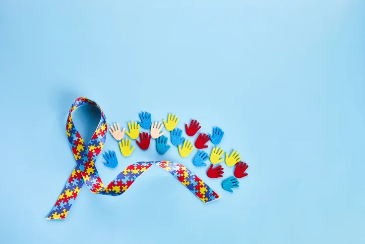 Autism awareness concept with colorful ribbon and hands on blue background. Top view