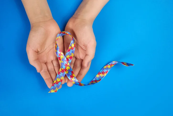 World Autism awareness day. Autistic boy hands holding puzzle pattern ribbon on blue background