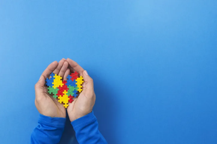 World autism awareness day concept. Child hands holding colorful puzzle heart on blue background