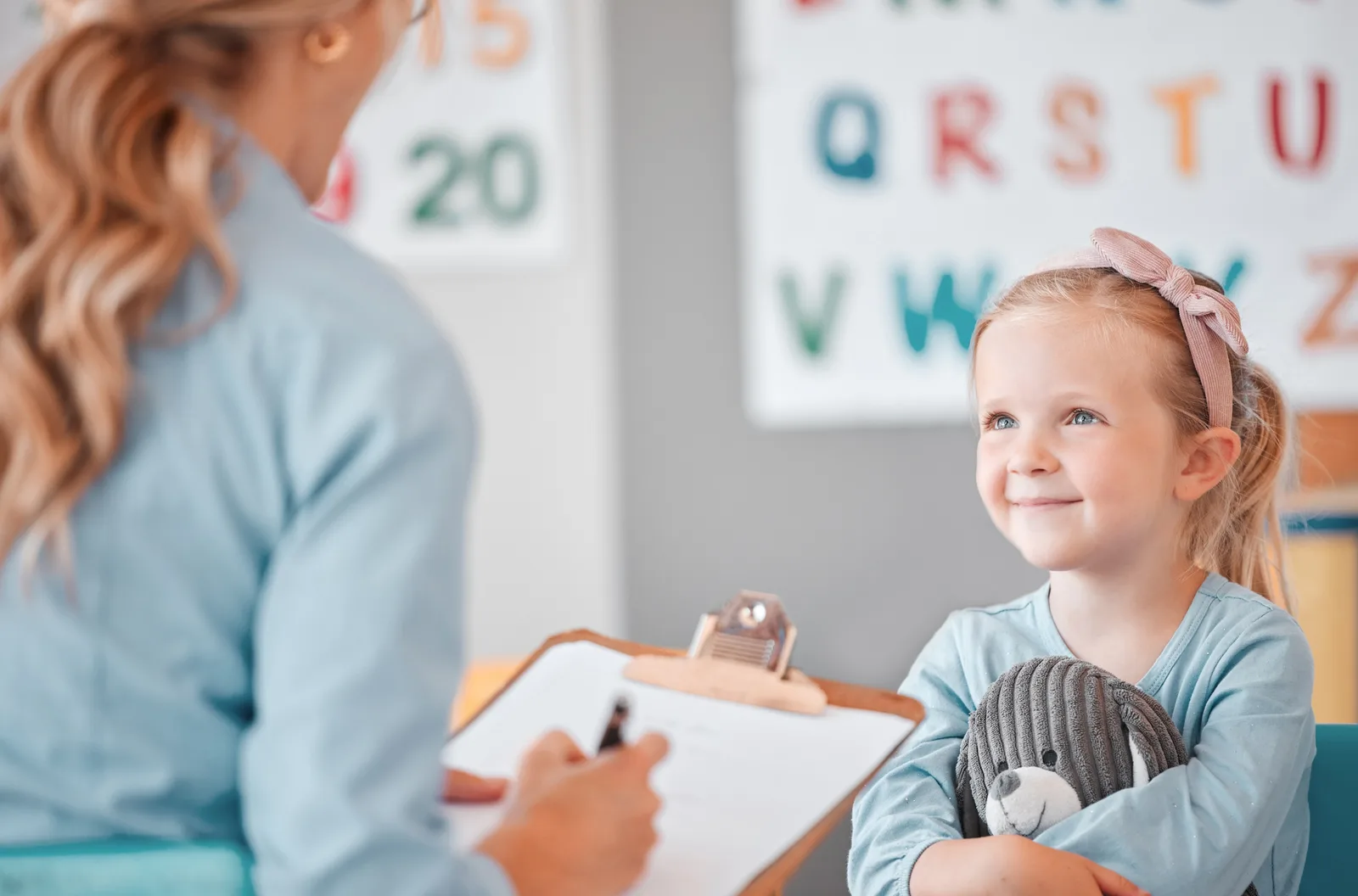 a little girl is sitting in front of a teacher holding a teddy bear