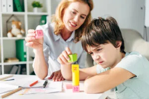 niño con dislexia y psicóloga infantil sonriente jugando con bloques de construcción