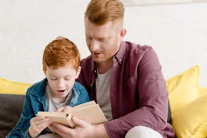 father looking at cute little son reading book at home