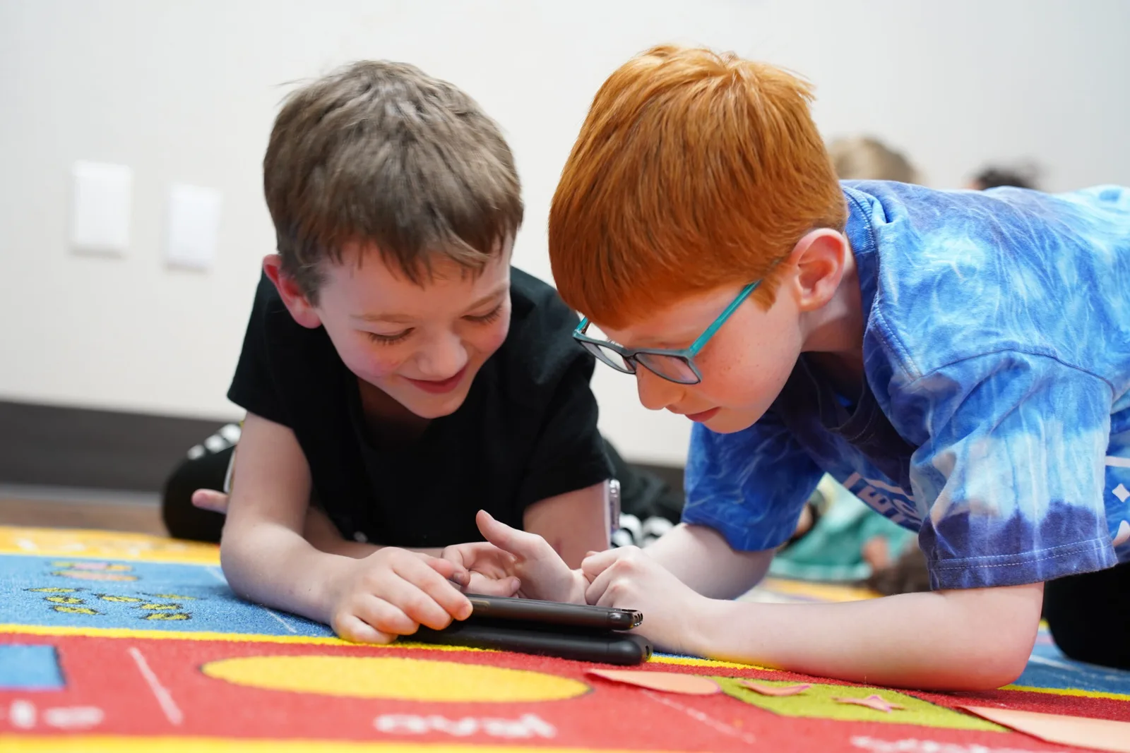 two boys laying on the floor looking at a tablet