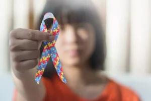 Niña autista sosteniendo un lazo que simboliza las piezas de un rompecabezas de colores para el día de la concienciación sobre las personas con trastorno del espectro autista en todo el mundo.