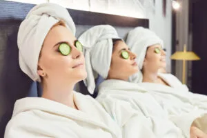 Chilling women in bathrobes with cucumber slices on face