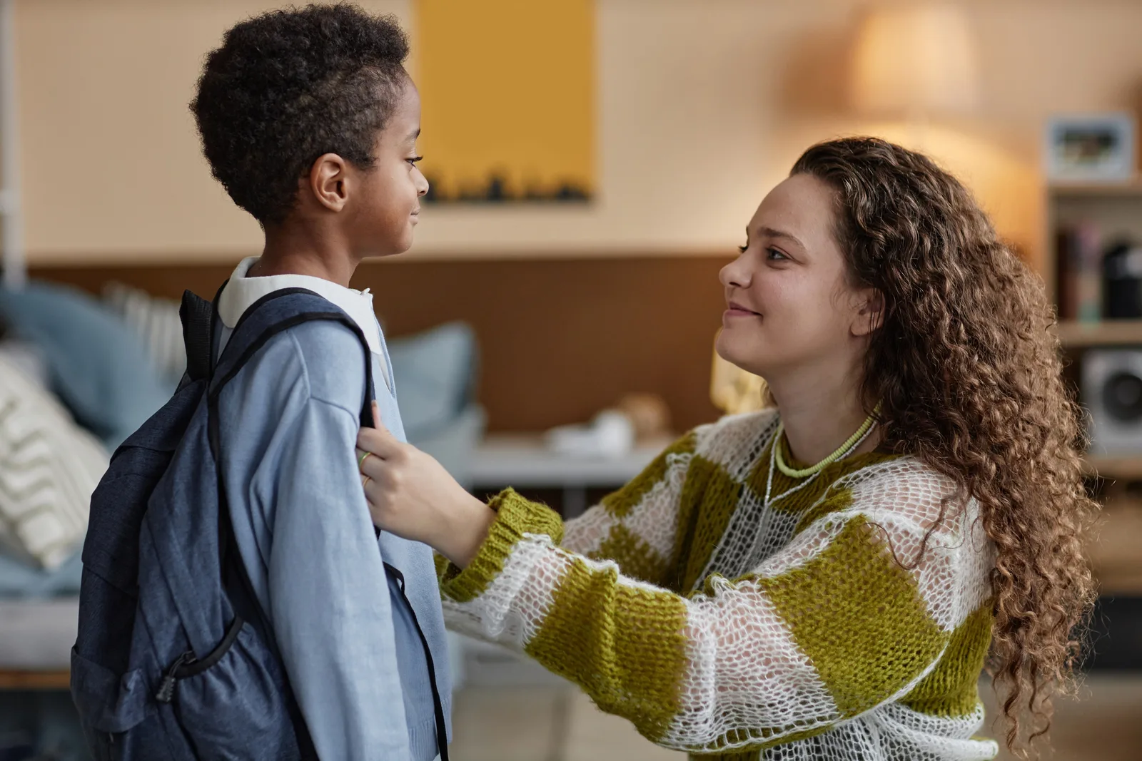 Parent helping a young child adjust a backpack before school