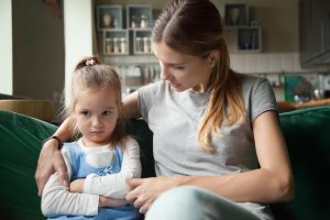 a woman sits on a couch with a little girl with her arms crossed