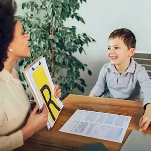 a woman is holding a clipboard with the letter r on it and talking to a young boy