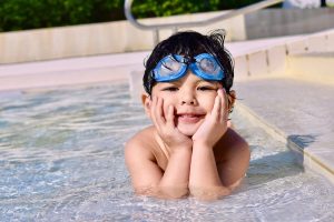 a young boy wearing goggles is laying in a swimming pool