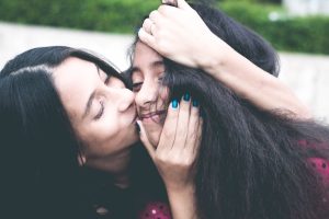 a woman with blue nails kisses her daughter on the cheek