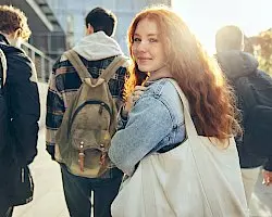 a group of young people with backpacks are walking down a sidewalk .