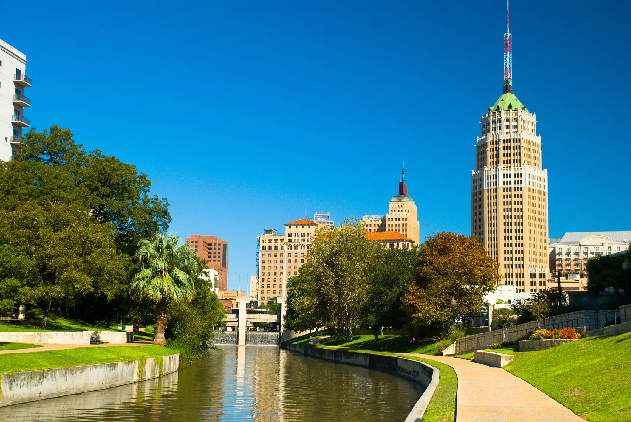 a river running through a city with a tall building in the background that says ' texas ' on it