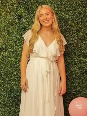 a woman in a white dress stands in front of a hedge wall