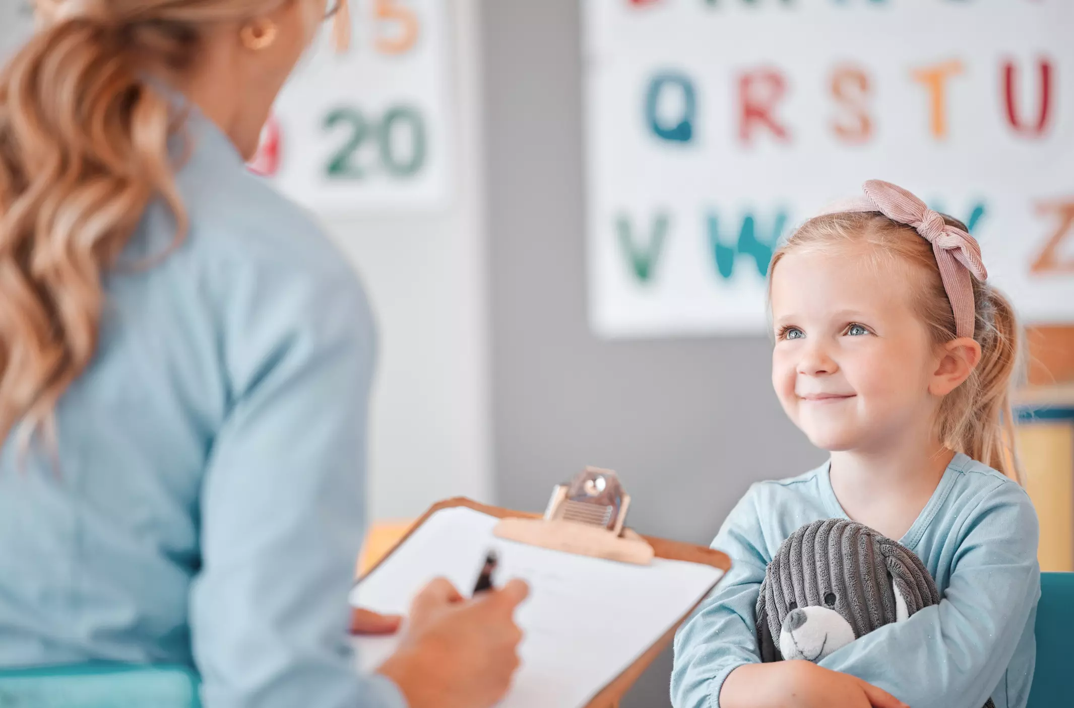 a little girl is sitting in front of a teacher holding a teddy bear