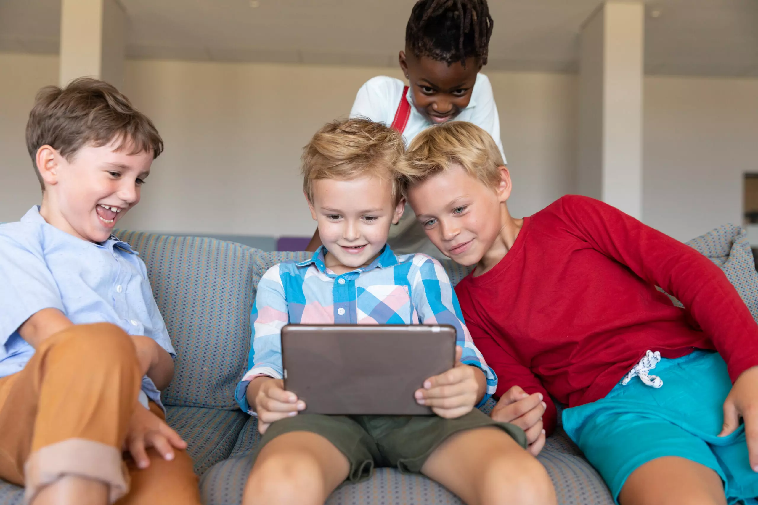 Smiling multiracial elementary schoolboys looking at digital tablet while sitting on couch in school