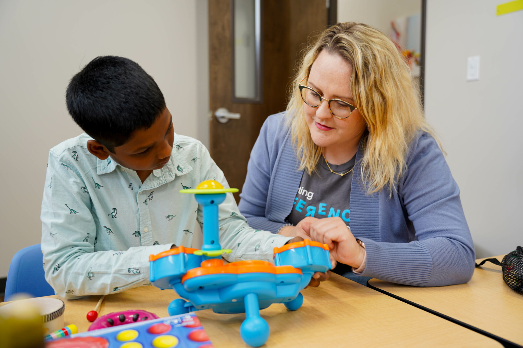 a woman and a boy are sitting at a table playing with a toy
