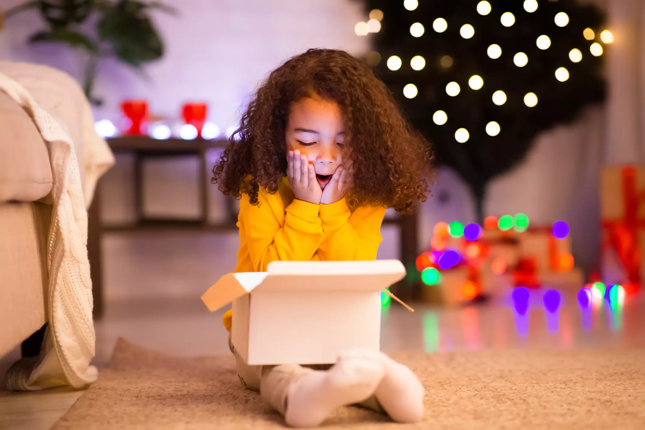 a little girl is sitting on the floor opening a gift box